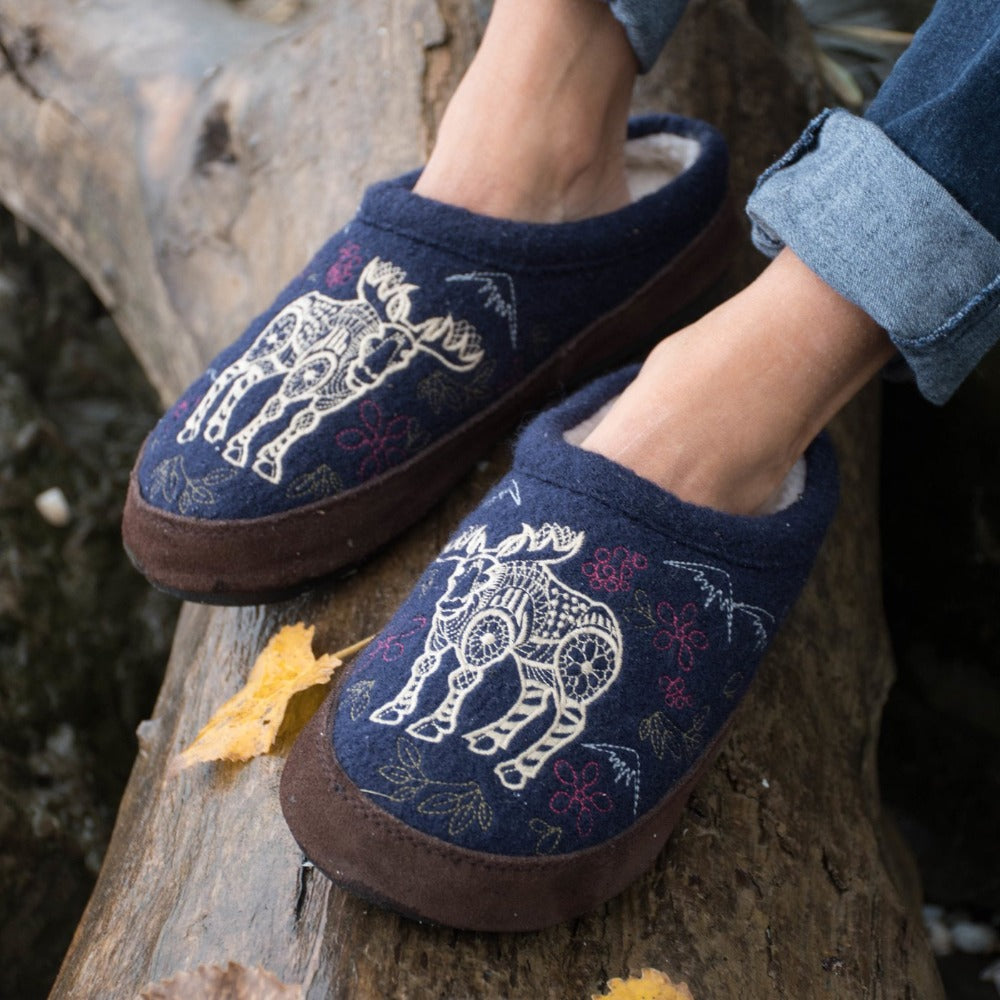 Women's Forest Mule Slippers in Navy Moose On Model Sitting on Log#color_navy-moose