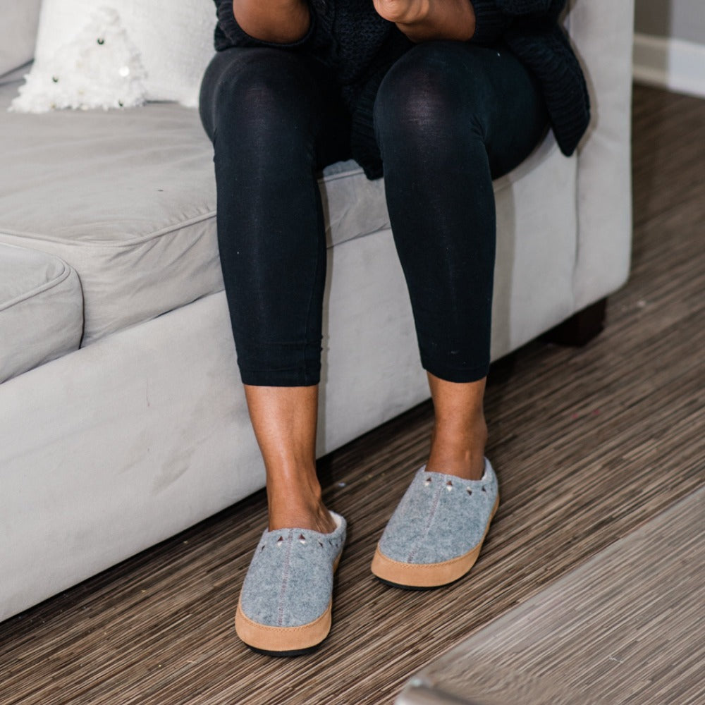 Women's Geo Embroidered Hoodback Slippers on figure wearing black leggings sitting on side of couch#color_ash