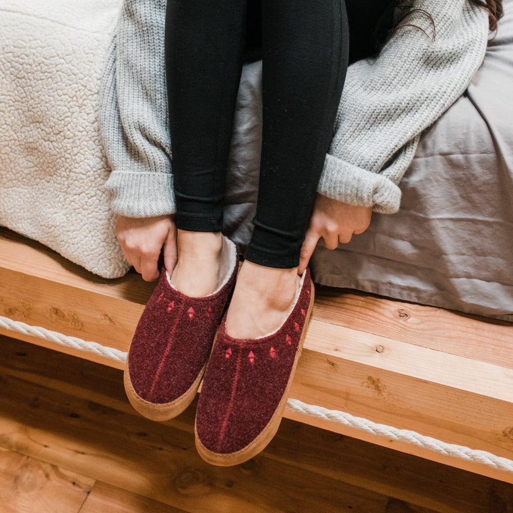 Women's Geo Embroidered Hoodback Slippers on foot sitting on the side of the bed with cozy sweater#color_garnet