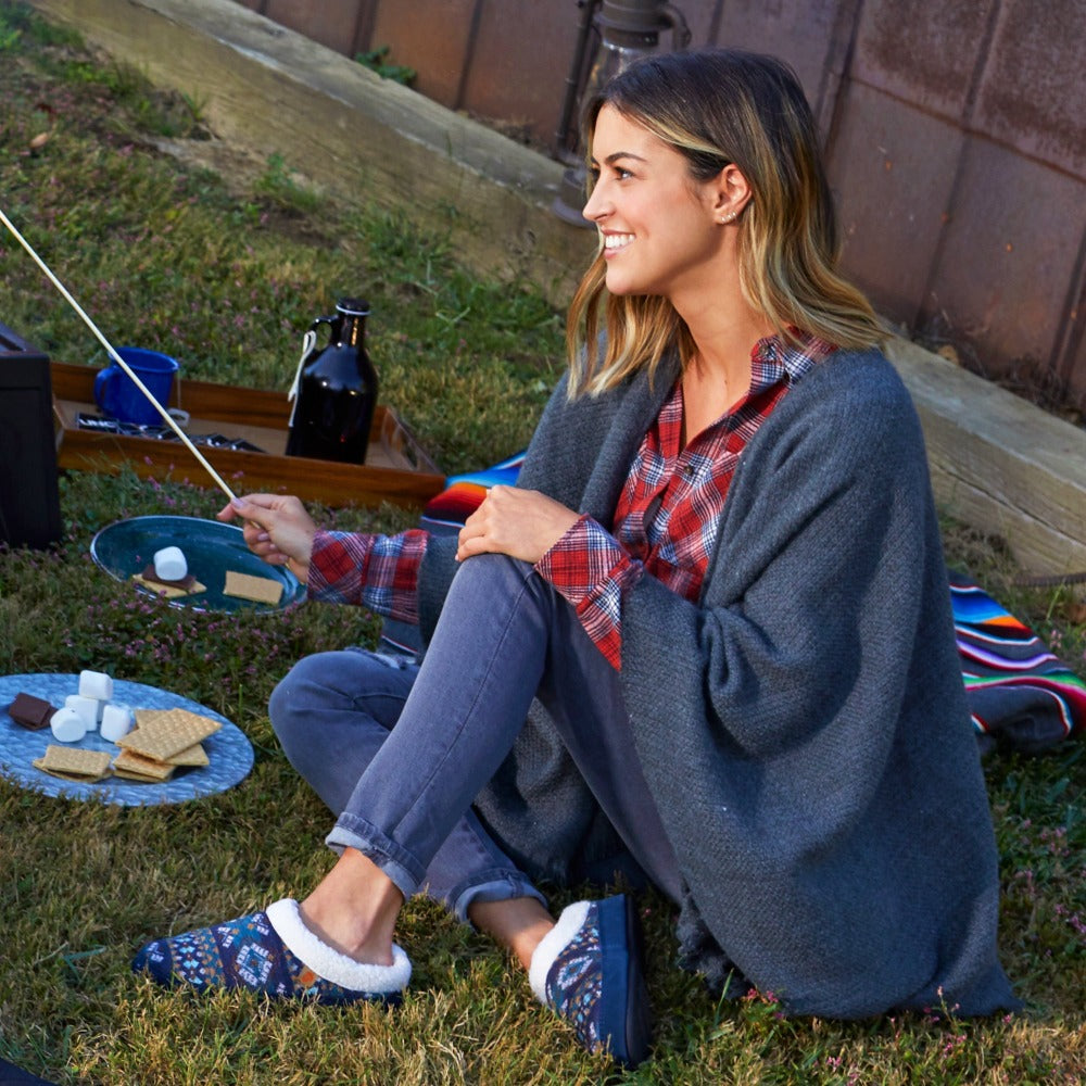 Women’s Fairisles Hoodback Slipper in Blue Multi with different hues of blue and tan on model sitting in front of a barn roasting marshmellows#color_navy