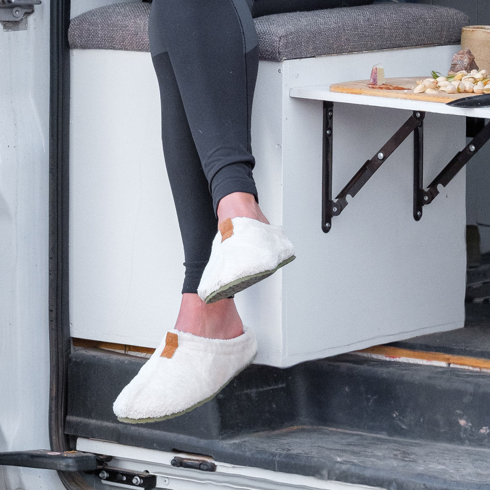 Women’s Algae-Infused Spa Slippers in Ewe on figure. Model sitting on seat in converted van with a charcuterie board next to her#color_white