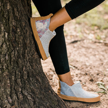 Women's Forest Bootie Slippers in Heather Grey Hare On Model Against A Tree#color_heather-grey-hare