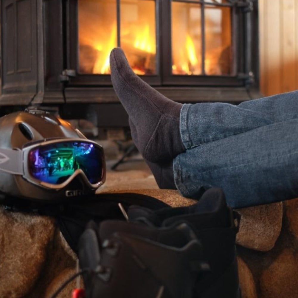 Man by Fire after Snowboarding in cozy cabin wearing charcoal versafit socks#color_charcoal
