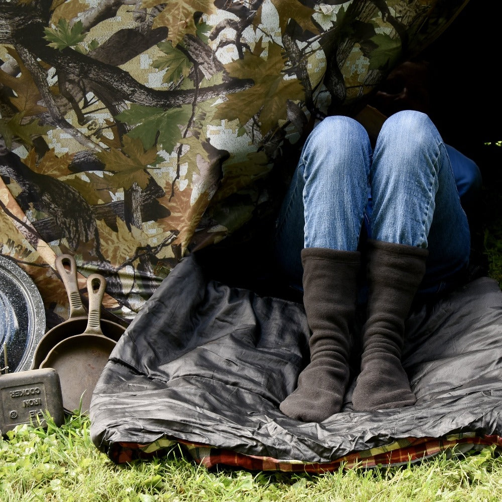 Versafit Fleece Cabin Socks in Black on-figure. Model sitting with their legs sticking out of a tent flap #color_black